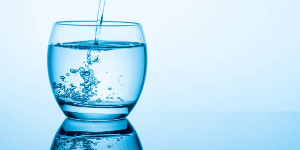 Flowing pure water into glass on blue background
