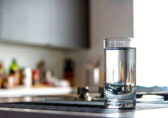 A glass filled with water atop a modern kitchen counter top inside a home.